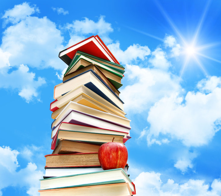Pile of books and apple against blue sky with sun and clouds