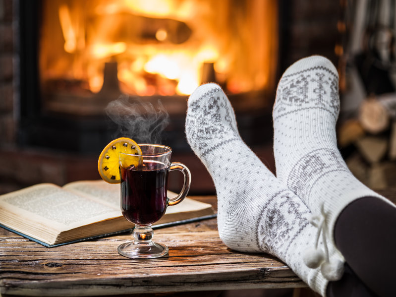 photo of warming and relaxing near fireplace. Woman feet near the cup of hot wine in front of fire.