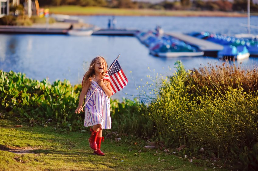 photo of young girl holding U.S. flag walking along waterfront