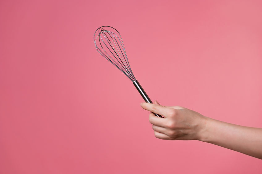 A woman's hand holding a kitchen whisk