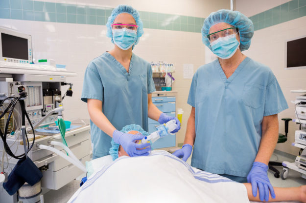 Portrait of nurses adjusting oxygen mask on female patient in operation room