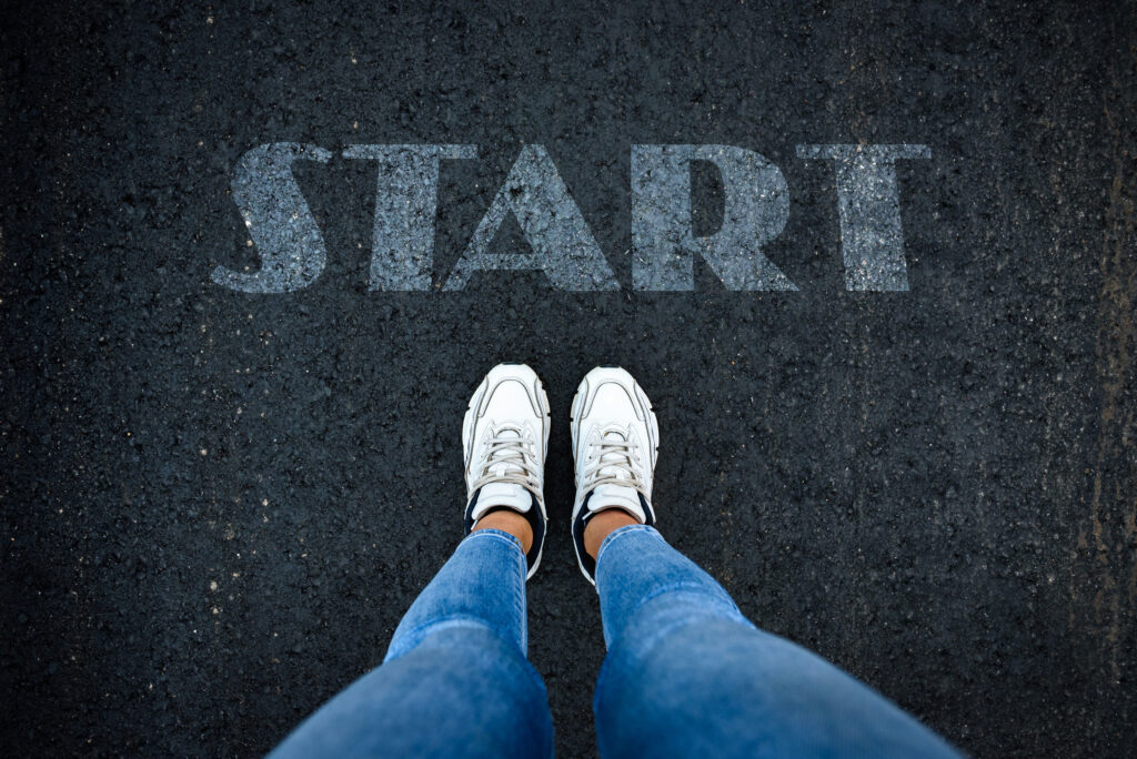 Female feet in white sneakers standing on street asphalt with word start written.