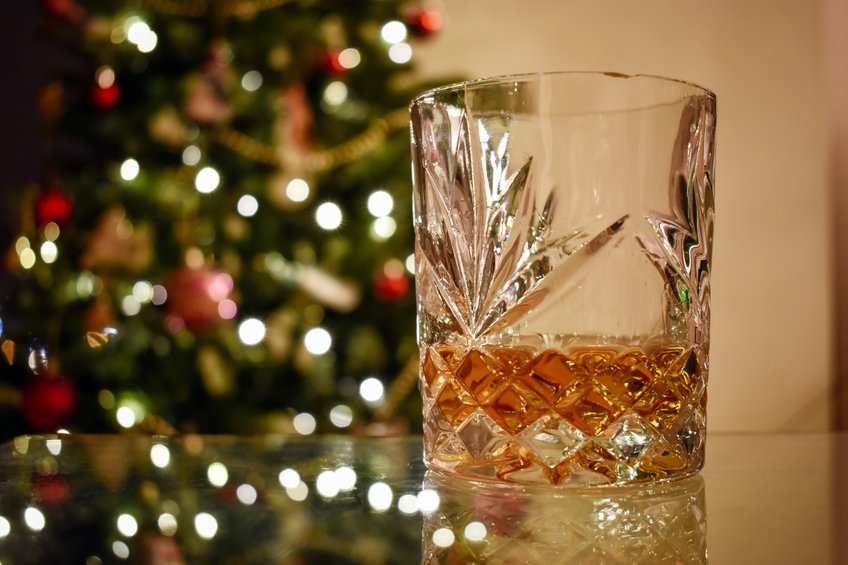 A close up of a festive glass of Whiskey on a glass table with a blurred Christmas tree in the background creating a festive atmosphere for the holiday season